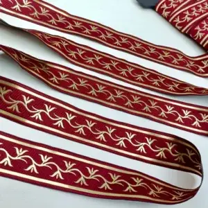 gerade-ausgelegtes-zierband-mit-rot-hintergrund-und-gold-gesticktem-rankenmuster-auf-transparentem-netzstoff-hintergrund
